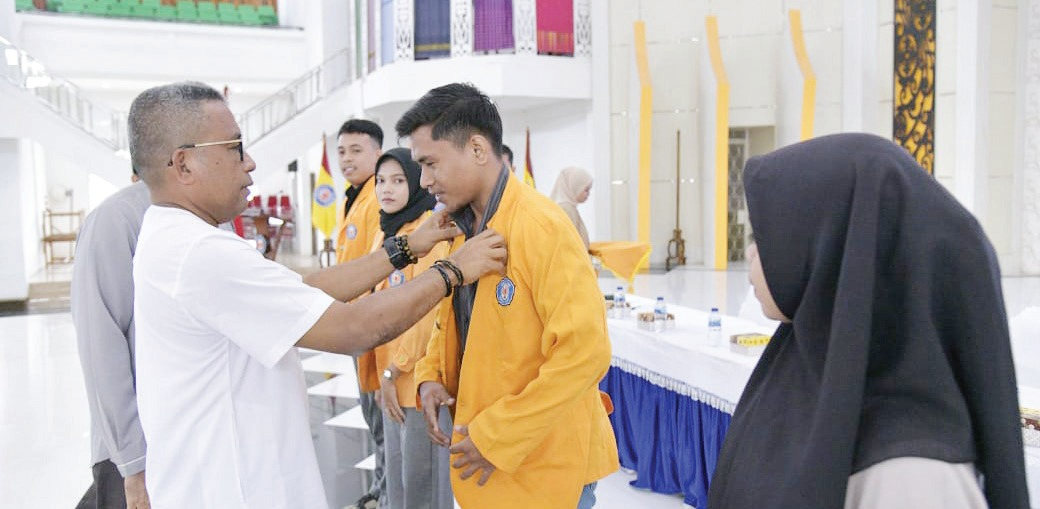 Rektor UHO Prof. Dr. Muhammad Zamrun Firihu, S.Si.,M.Si.M.Sc (kiri) menyematkan almamater UHO kepada perwakilan mahasiswa KKN dalam seremoni pelepasan di Auditorium Mokodompit UHO, Jumat (9/8/2024).(HUMAS UHO)