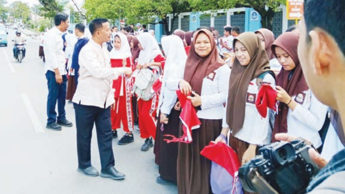 BAGI-BAGI BENDERA : Kepala Dinas Dikbud Sultra,Yusmin (depan kiri) didampingi Kepala SMA Negeri 1 Kendari, Ruslan (depan kanan) bersama siswa SMA/SMK membagikan bendera merah putih kepada masyarakat di sekitar kantor Dikbud Sultra, Jumat (2/8).(RAHMA SAFITRI/KENDARI POS)